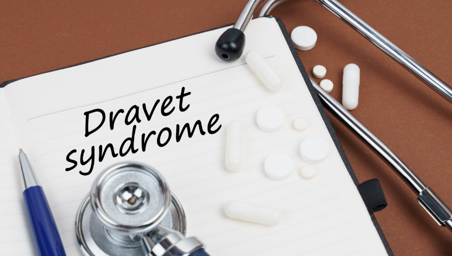 Notizbuch mit der Aufschrift „Dravet syndrome“, Stethoskop und Tabletten darauf.